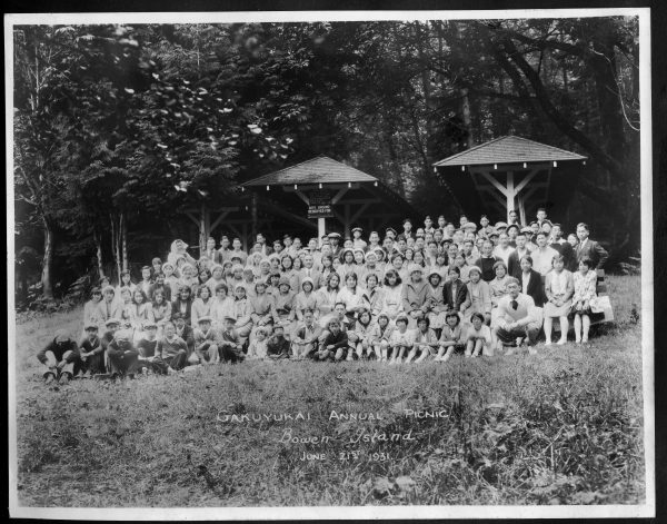 A gathering of over 100 people sitting closely together near covered picnic stands. A handwritten caption reads "Gakuyukai Annual Picnic, Bowen Island, June 21st, 1931"